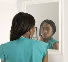 Coloured image of a woman looking at her reflection in a mirror, she looks sad
